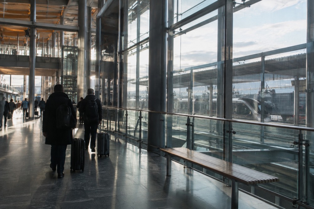 A modern airport terminal hall with a train platform visible through glass walls
