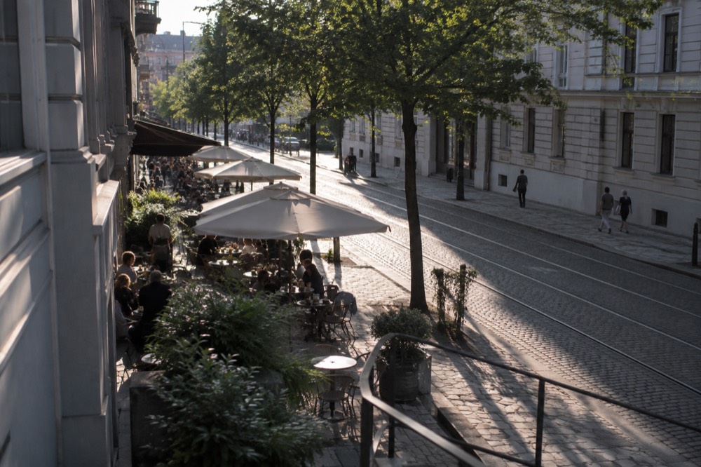 Outdoor cafe tables along a cobblestone Oslo street in summer light