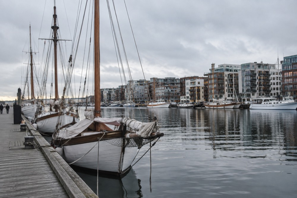 Wooden sailing boats moored at a harbor pier with apartment buildings behind