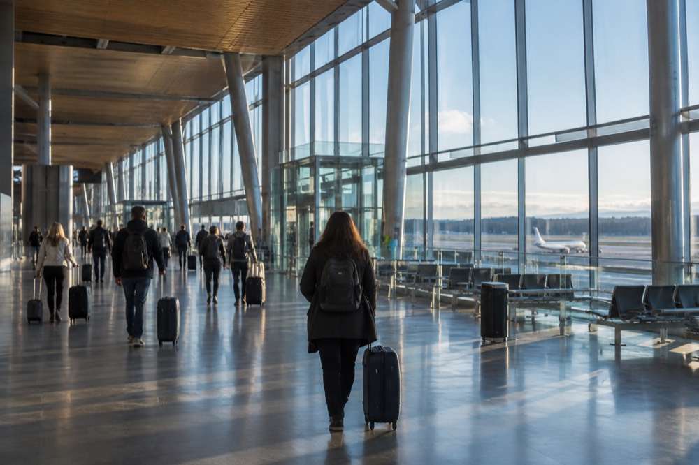 Modern airport terminal interior with tall windows and passengers walking toward departure gates
