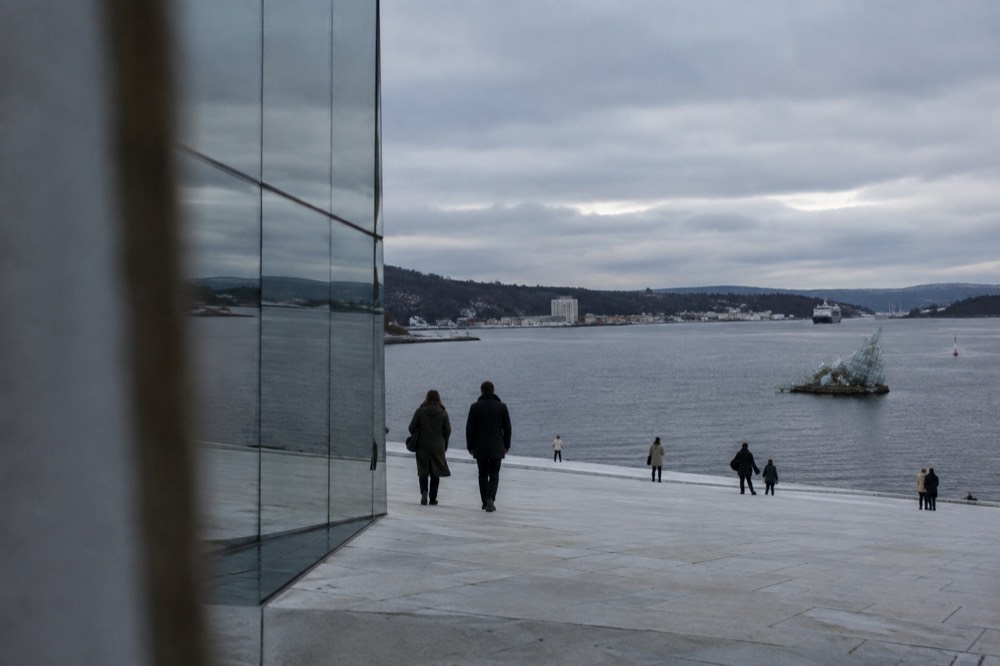 People walking on the sloping marble roof of the Oslo Opera House with the fjord behind