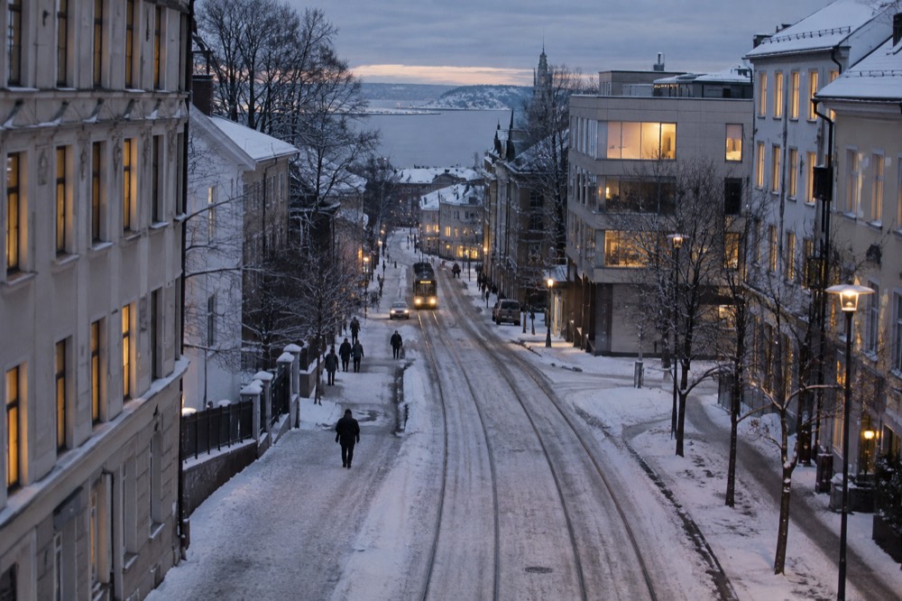 Snow-covered street in Oslo with warm window light during blue winter twilight