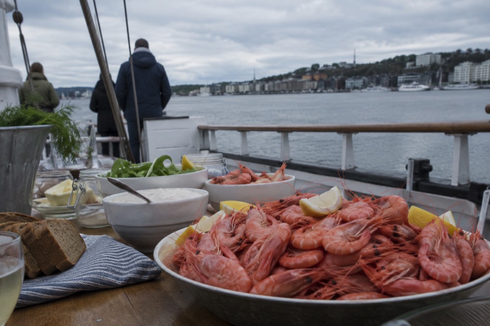 White shrimp buffet spread on a boat table with the Oslofjord shoreline behind