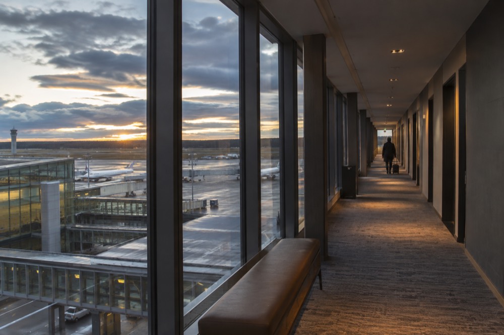 A hotel corridor with tall windows looking out over a modern airport terminal at dusk