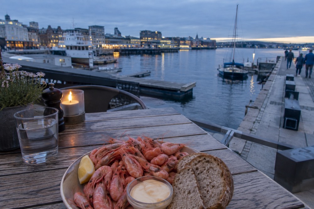A plate of fresh fjord shrimp with bread and lemon on a wooden table by the Oslo waterfront