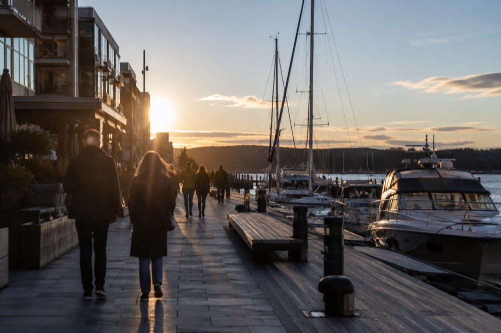 People walking along the harbor promenade with boats moored at Aker Brygge
