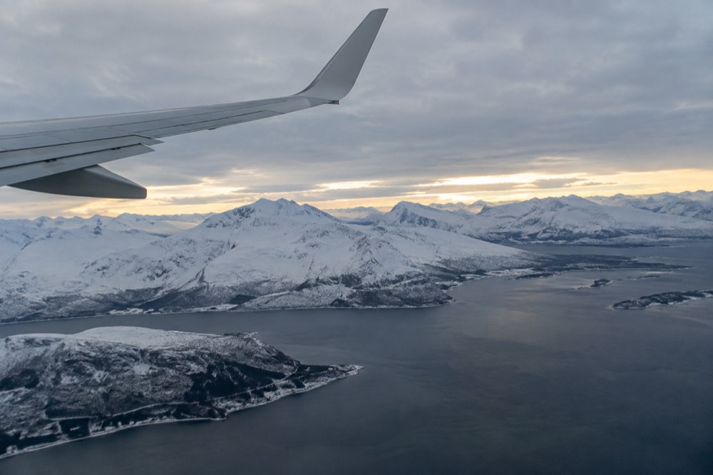 Aircraft wing above snow-covered Norwegian mountains on approach to a northern airport