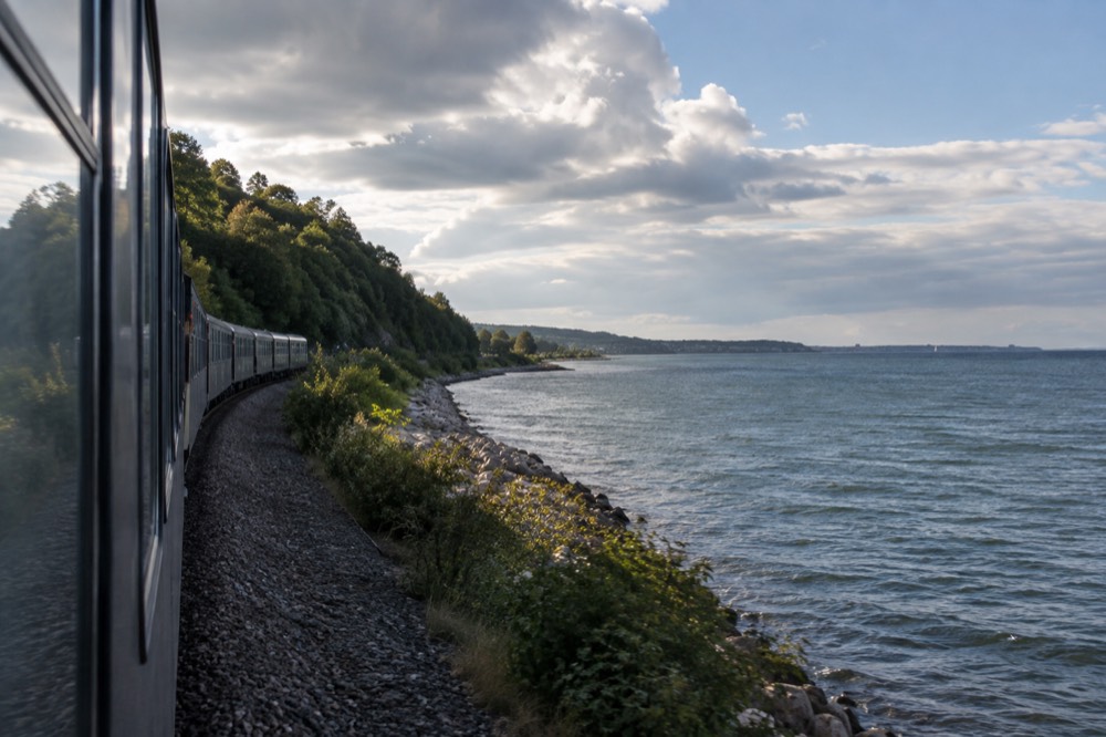 A passenger train traveling along a forested coastline in Scandinavia