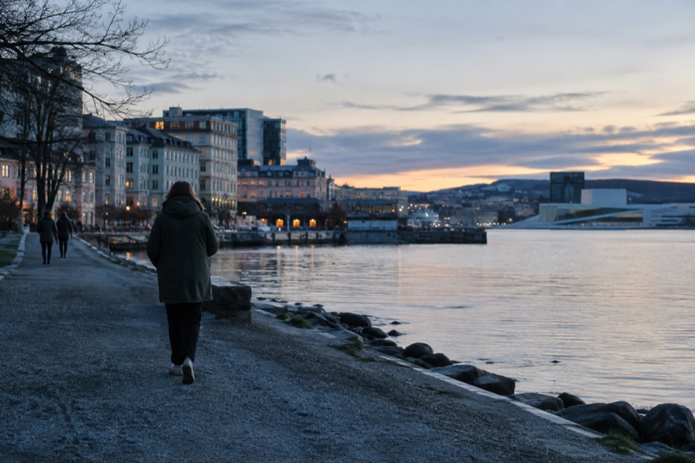 Person in a rain jacket walking a gravel path beside the Oslofjord
