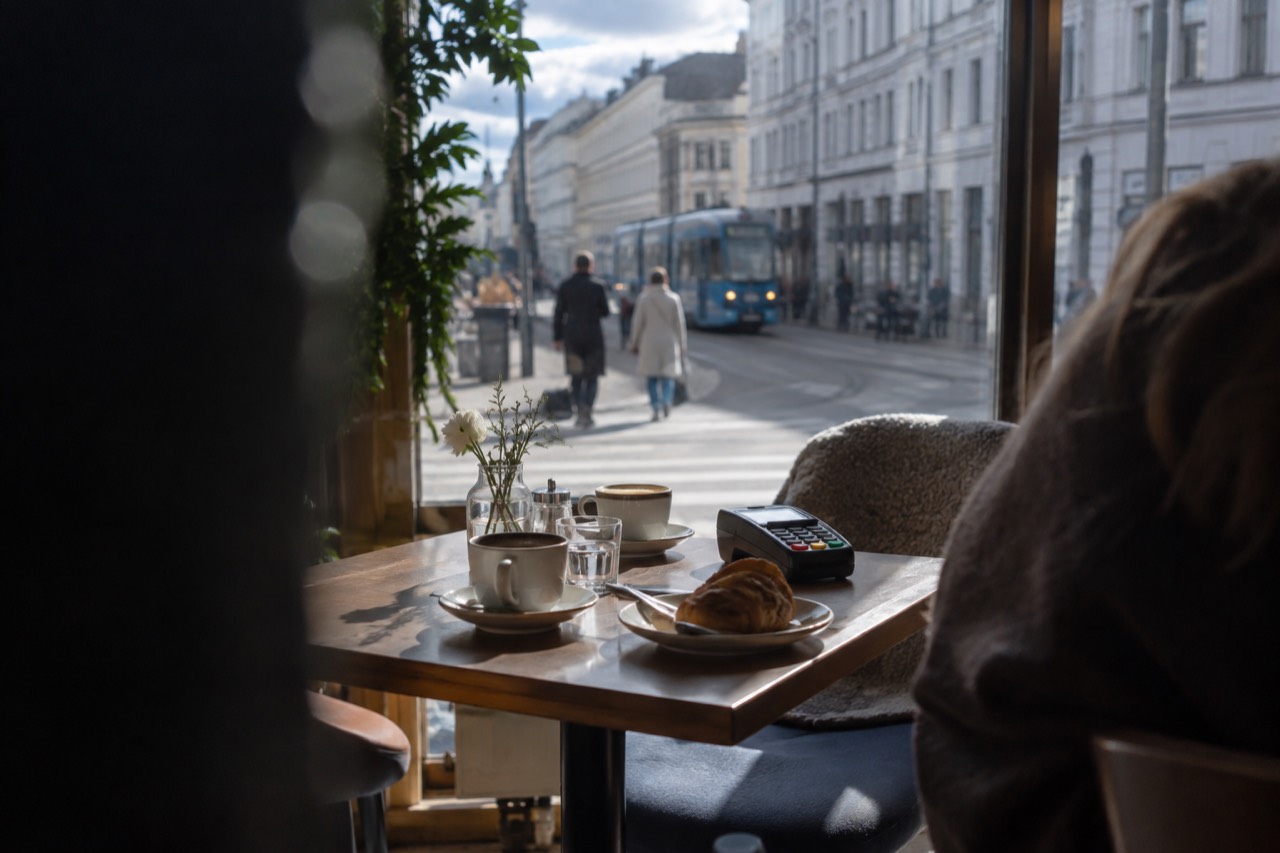 A set table with a card terminal beside coffee cups in a bright Oslo restaurant