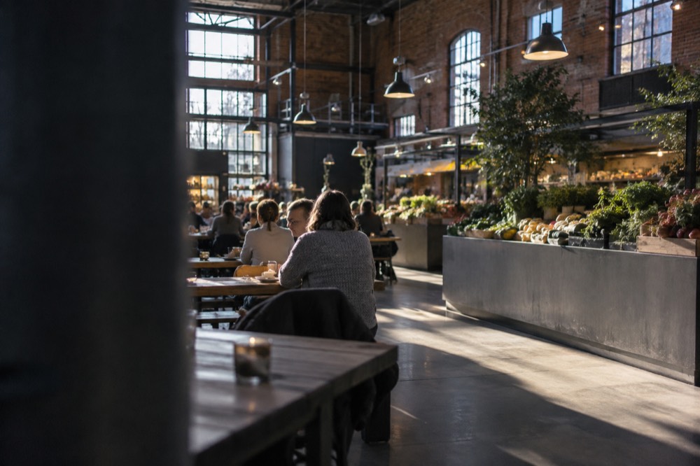 People sharing food at long wooden tables in a warm Oslo food hall