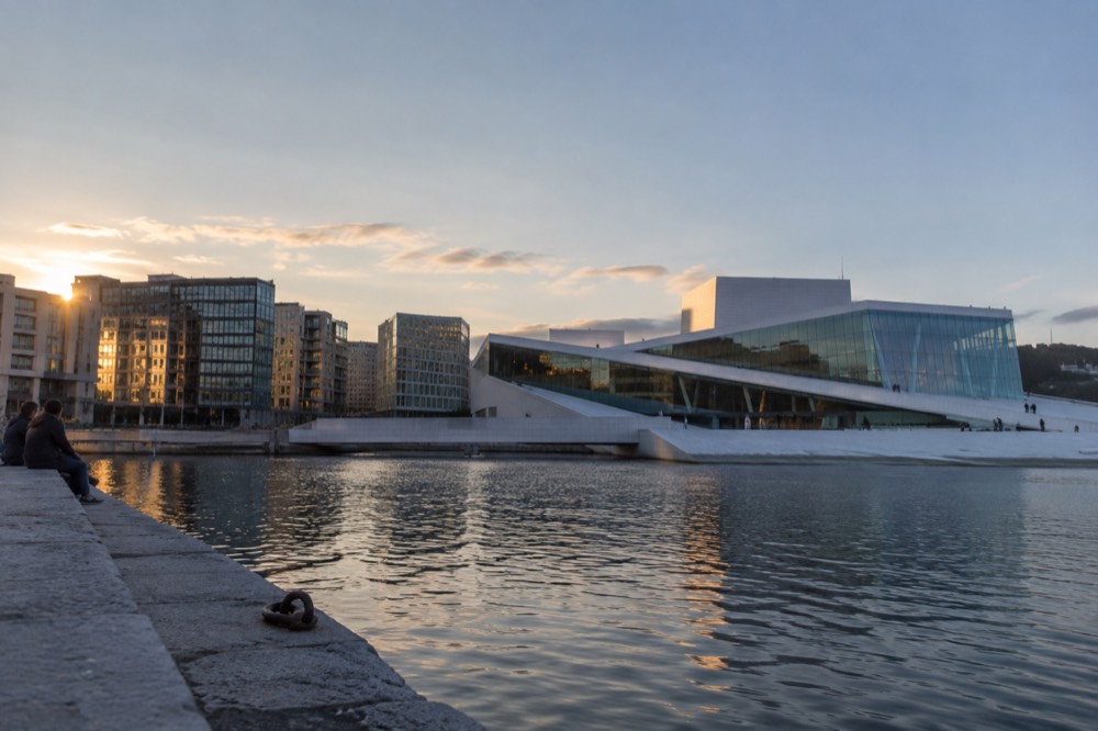 A city waterfront at dusk with a modern opera building and calm water