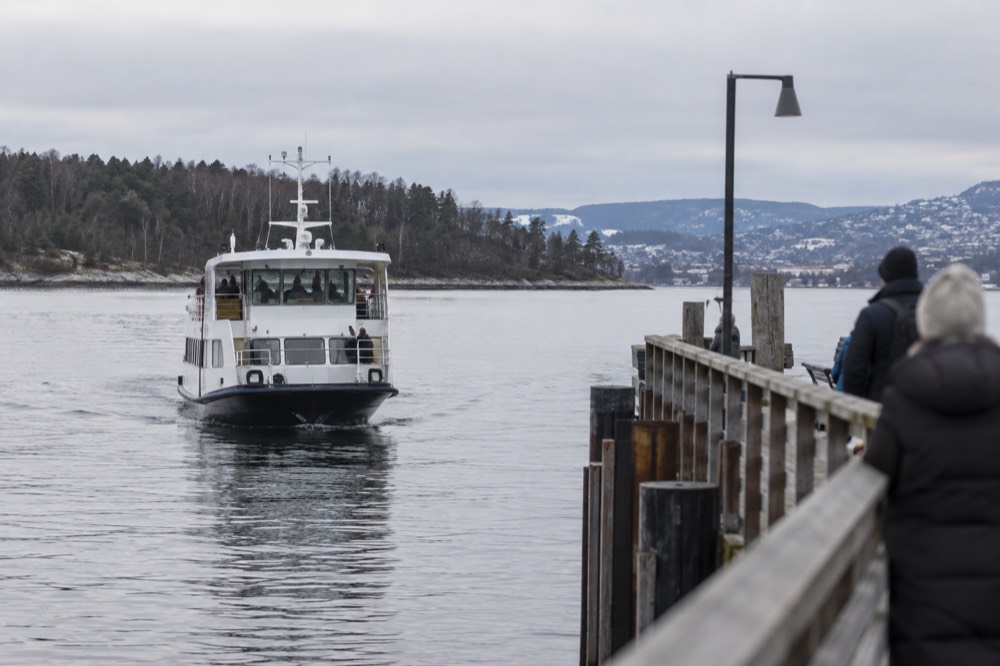 A small passenger ferry approaching a wooden pier on a calm fjord