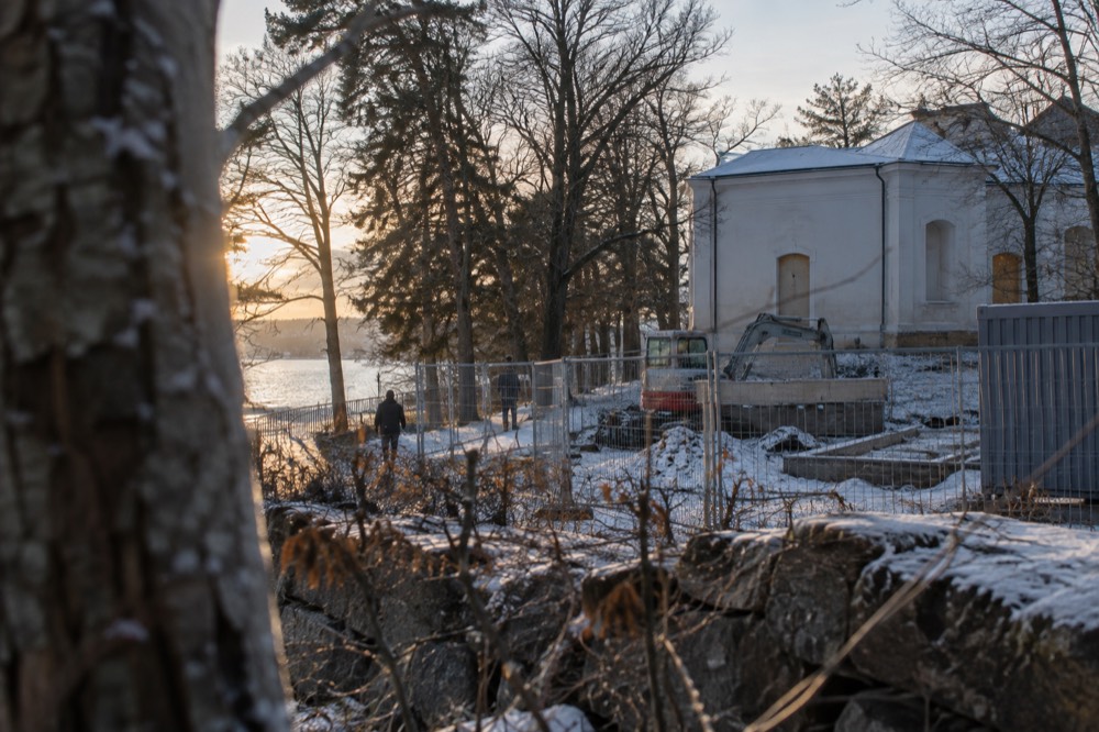 A fenced construction site beside a closed museum building among trees