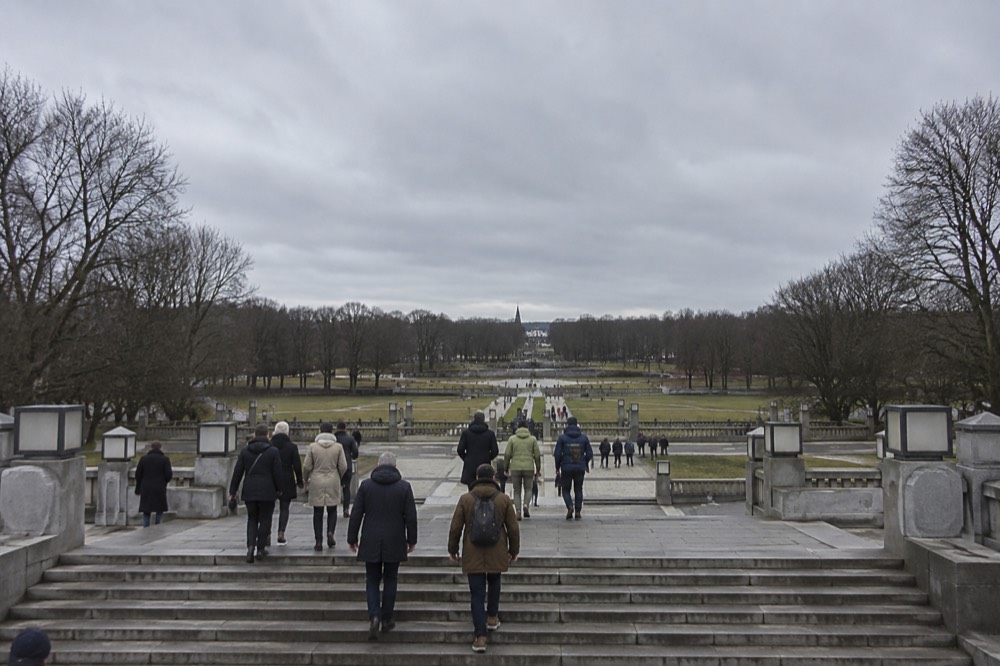 Wide stone stairway rising through Vigeland Park with visitors climbing between trees