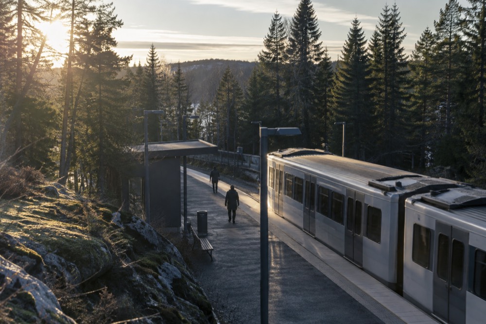 A metro platform at a forested hilltop station with pine trees behind it