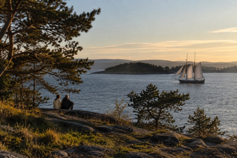 Traditional wooden sailing ship with masts underway on the fjord near islands