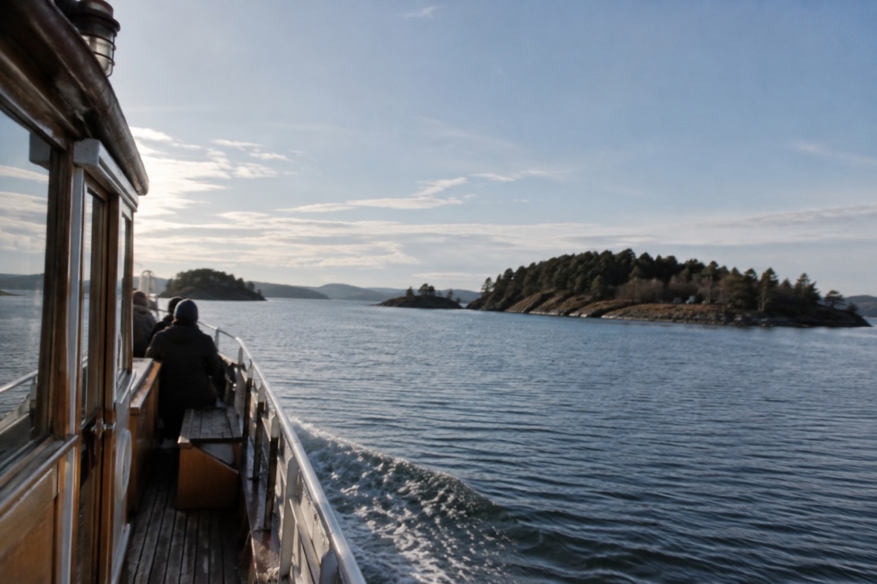 Wooden ferry departing a city pier toward small green islands across calm fjord water