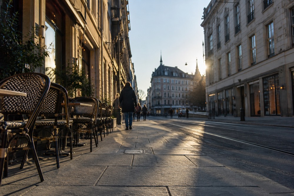 A pedestrian shopping street with outdoor cafe tables and historic buildings