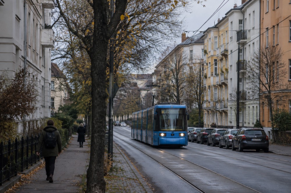 A tram line running along a city street with apartment buildings and trees