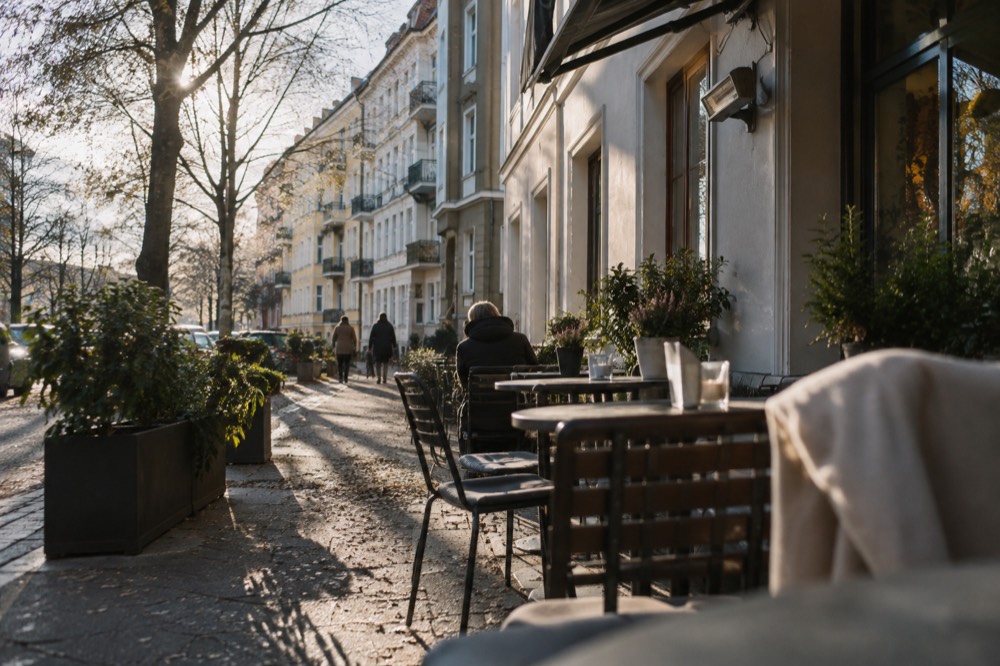 A café terrace on a quiet residential street with outdoor tables and trees