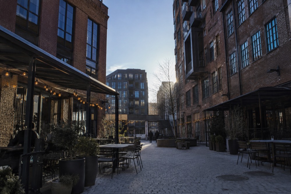 A brick courtyard between converted industrial buildings with outdoor tables and string lights