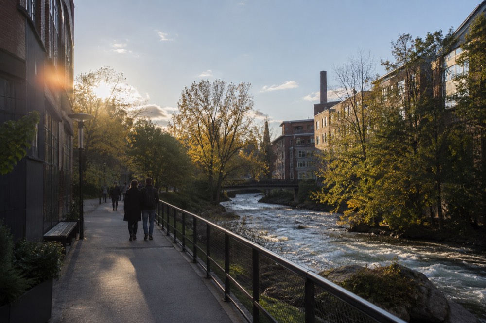 A paved riverside path beside a fast flowing urban river with trees on both banks