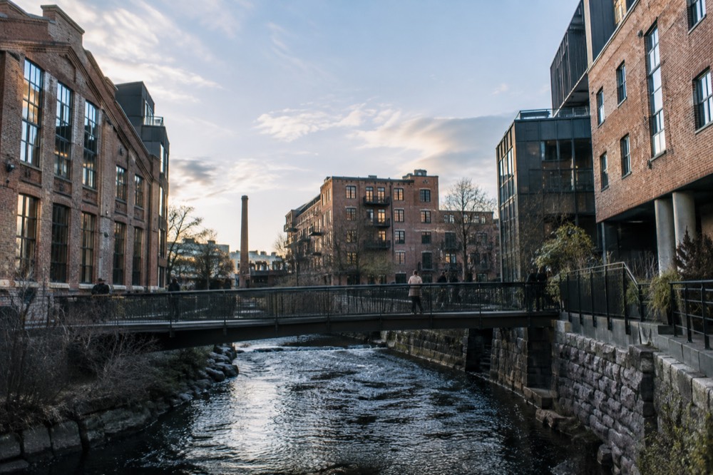 A modern footbridge crossing a river between old brick factory buildings