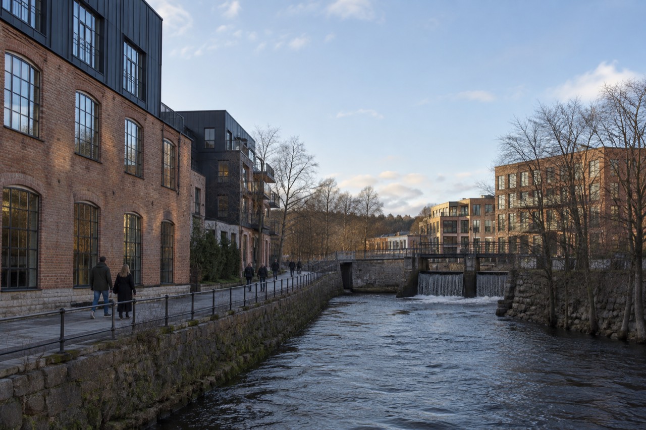 A converted industrial brick building beside a river in Oslo with people walking along the waterfront