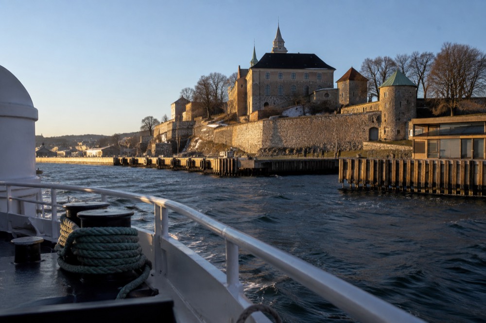Passenger ferry approaching a wooden pier with fortress walls rising behind