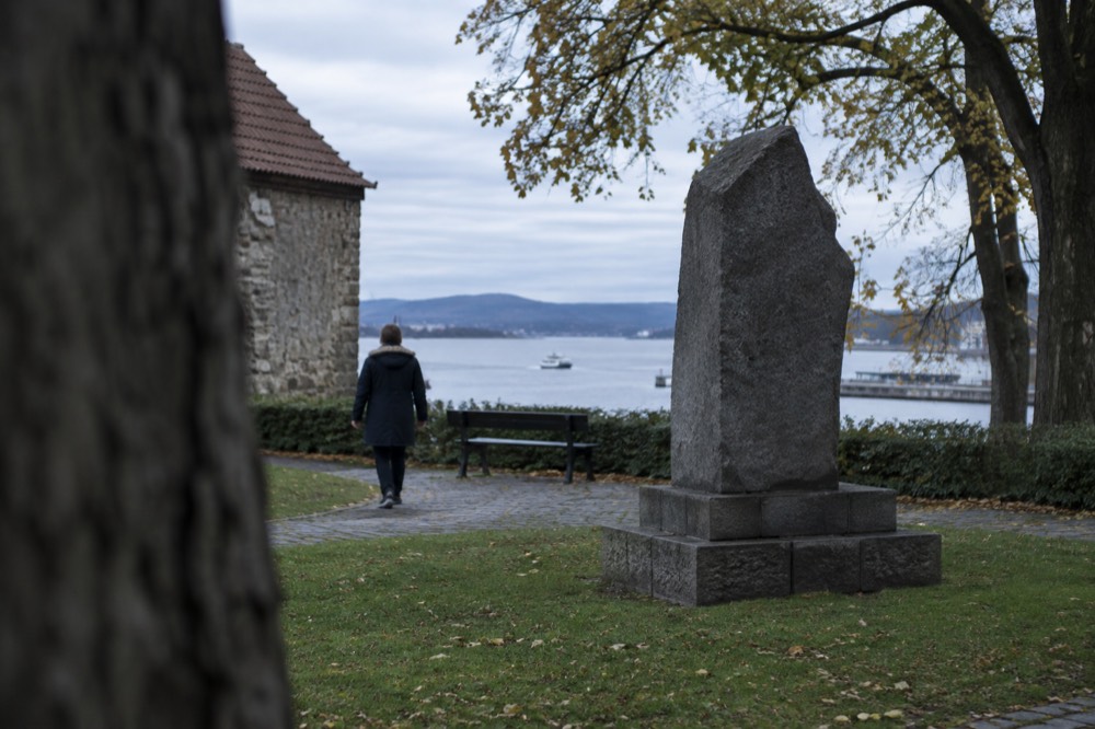 Stone memorial in a quiet green corner of the fortress grounds with the fjord beyond