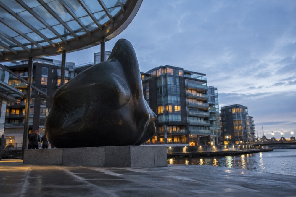 Outdoor sculpture beside a canal with apartment buildings behind