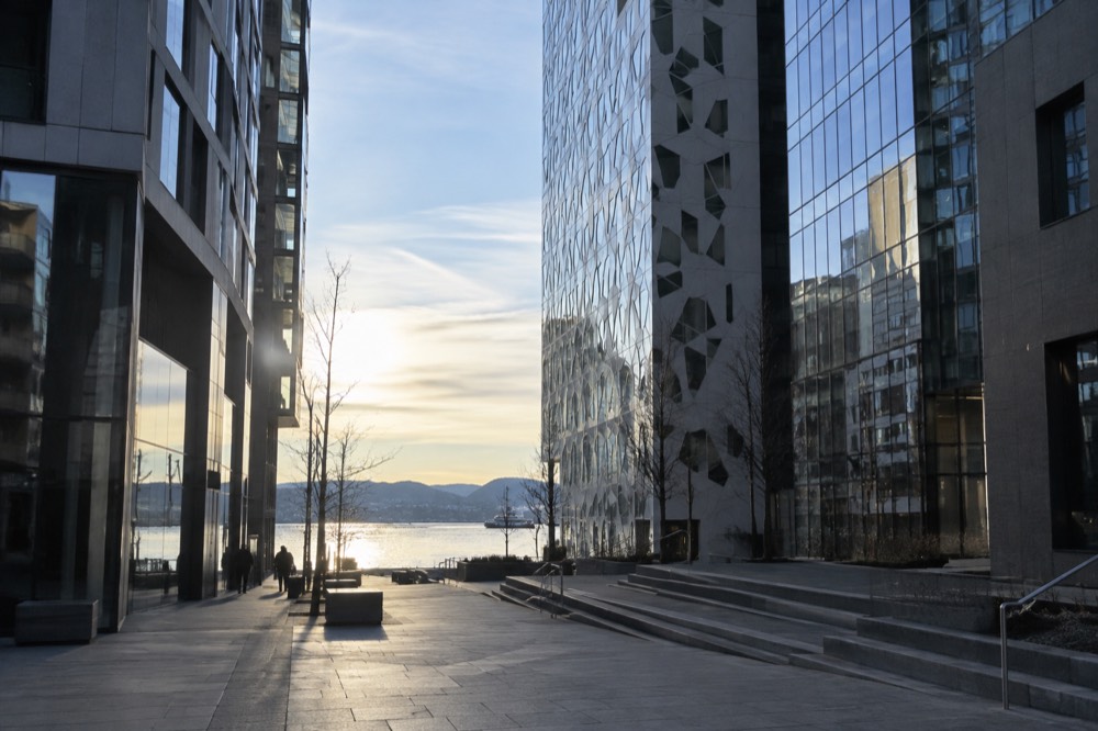 Narrow glass towers standing close together with a fjord visible in the gap between them