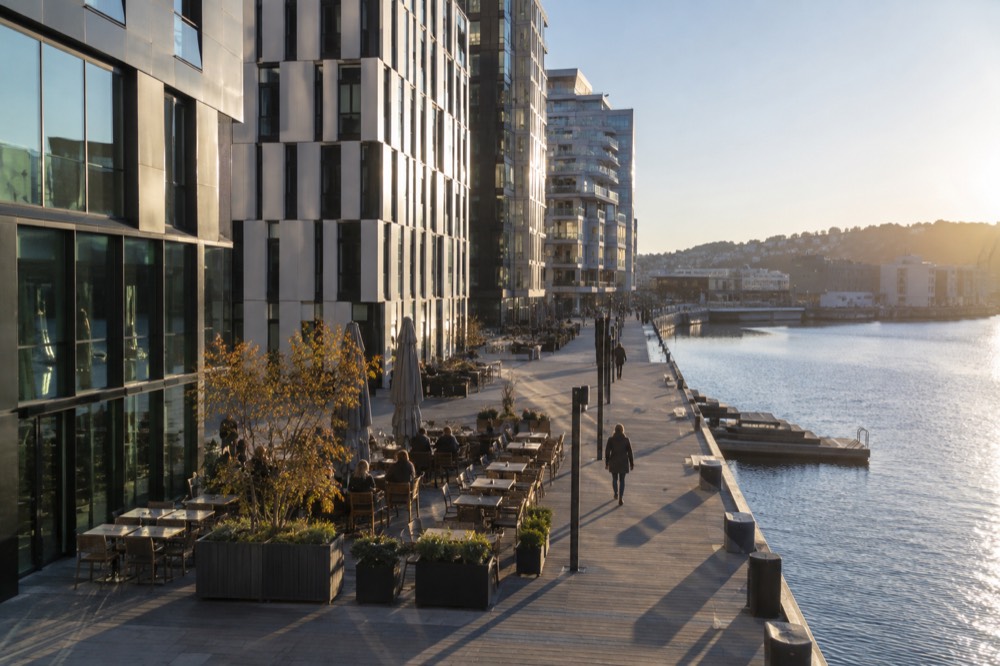 Outdoor restaurant tables set along a waterfront boardwalk between modern buildings