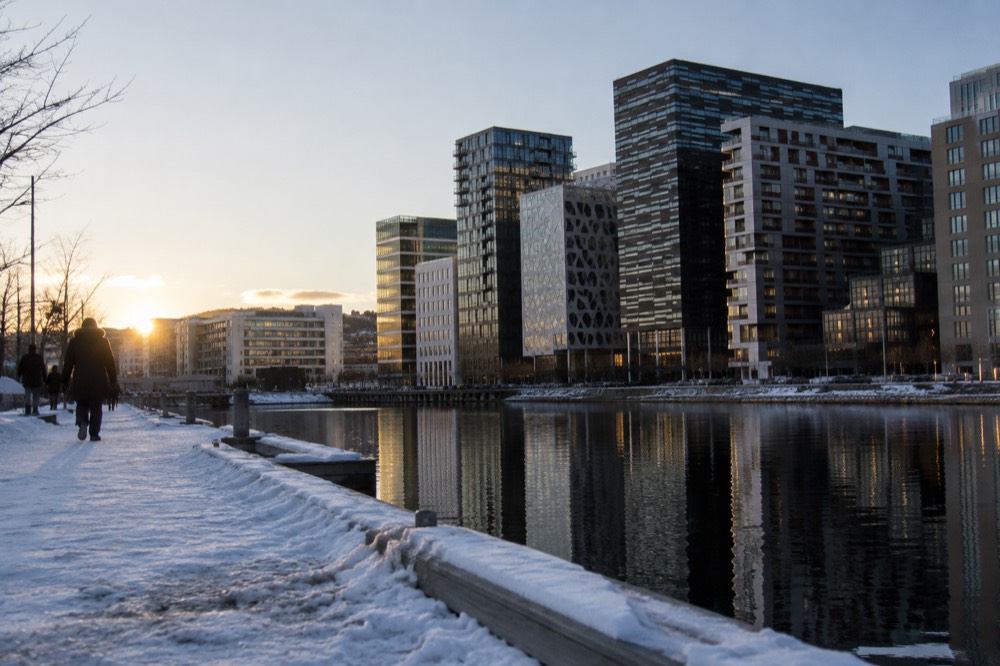 Illuminated glass towers reflecting in dark fjord water on a winter evening