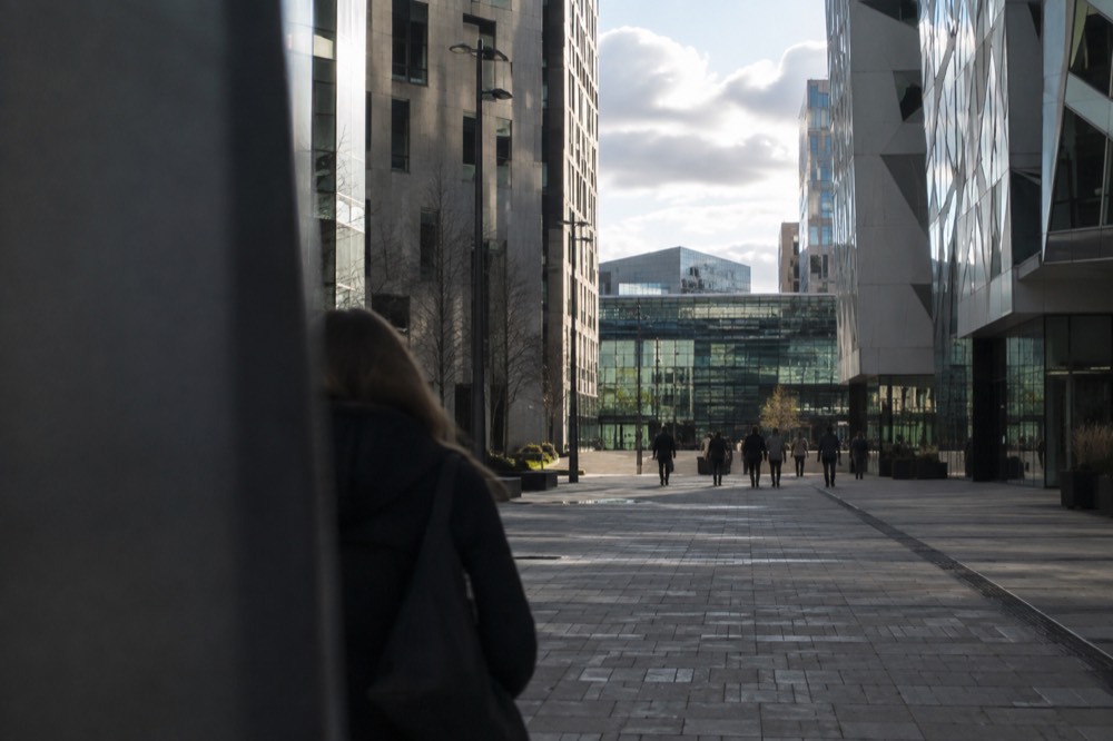 Pedestrian street between modern towers leading toward a glass station facade