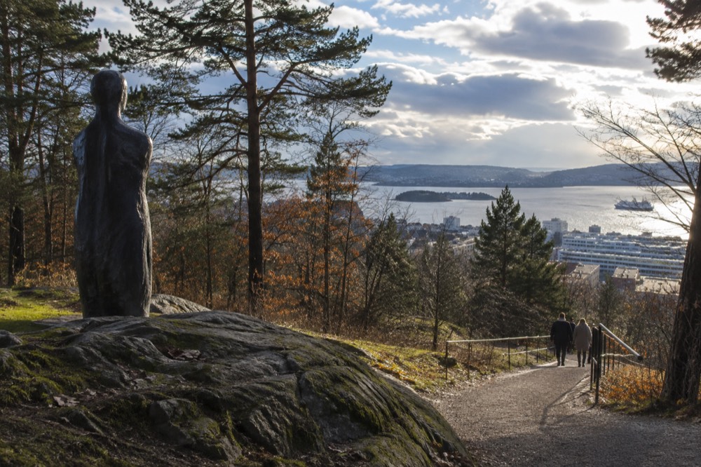Wooded hillside path with sculptures overlooking the Oslofjord and city rooftops
