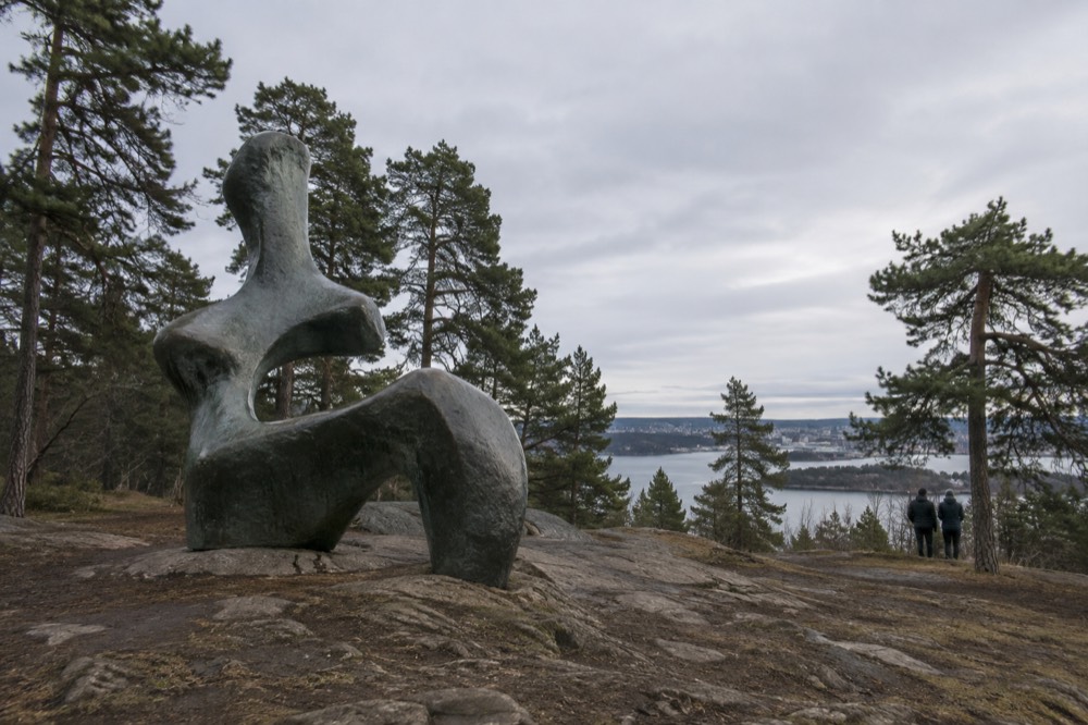 Large abstract sculpture standing in a woodland clearing with pine trees