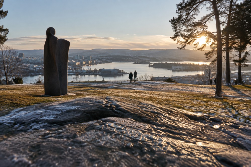 Open lawn with sculptures and city skyline beyond the fjord