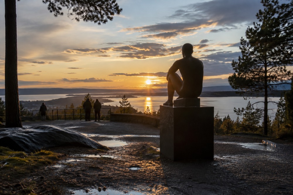 Sculpture silhouetted against a low golden sun over the fjord