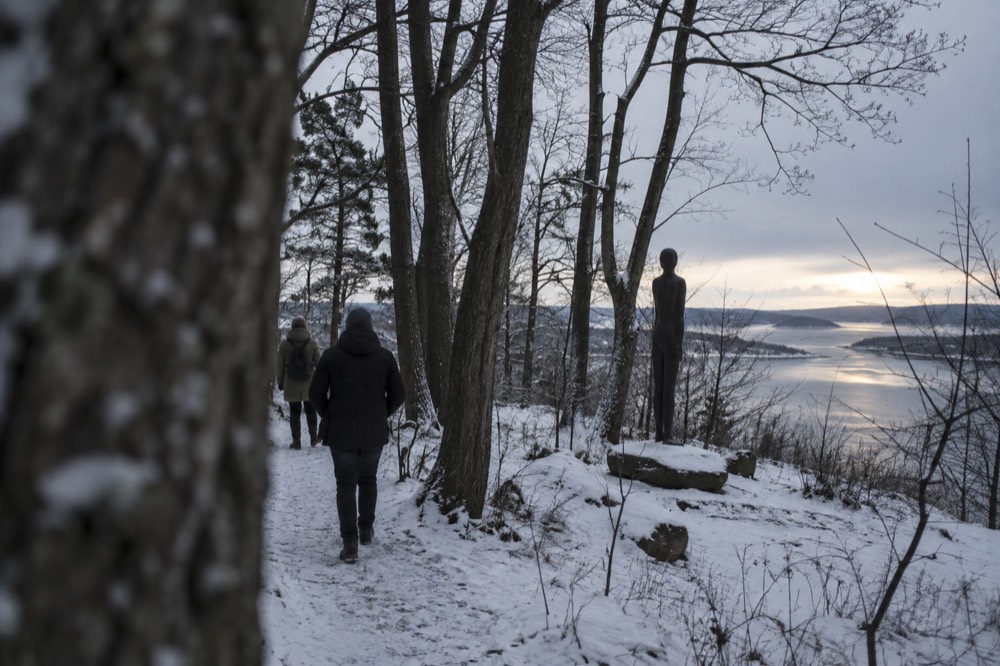 Snow-dusted forest path with a dark sculpture visible between trees