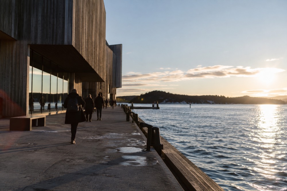 Museum visitors reading expedition exhibits arranged around a massive wooden ship hull