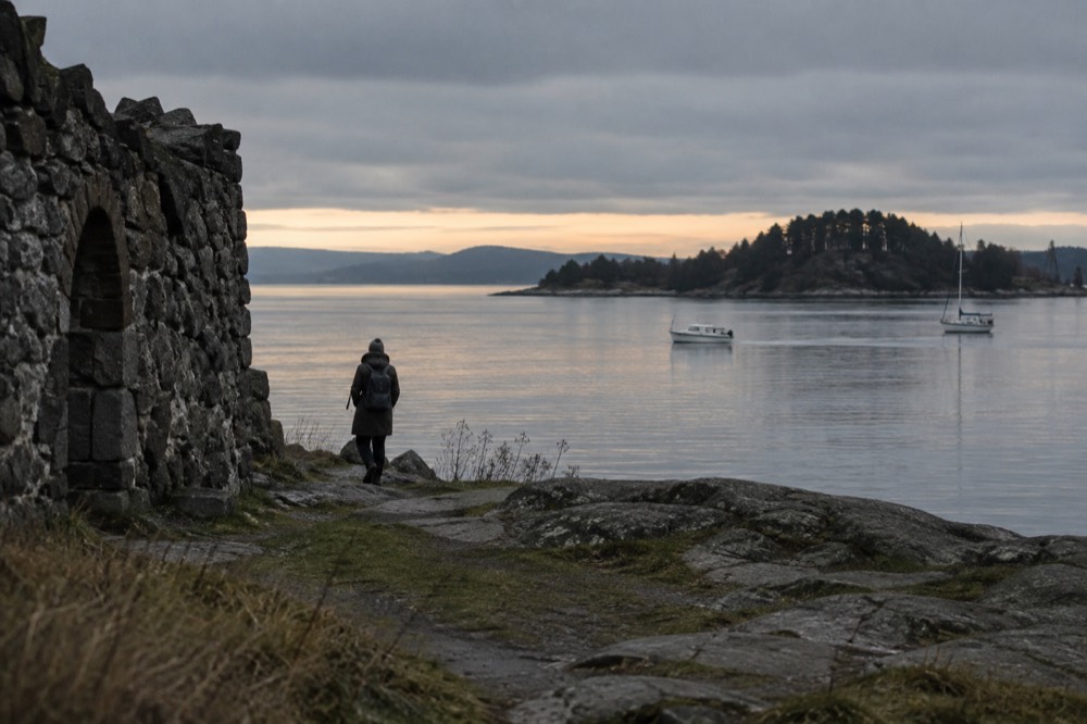 Evening light over calm fjord water with an island silhouette and small boats