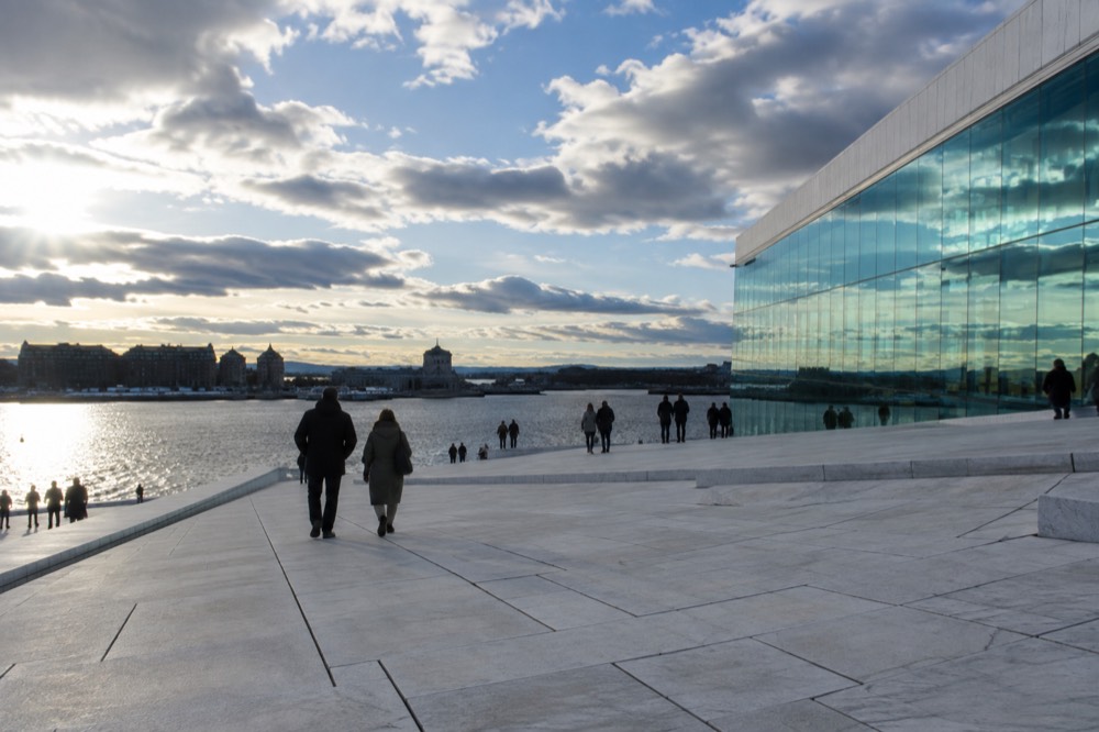 Sloping white marble roof of a waterfront opera house with people walking on it