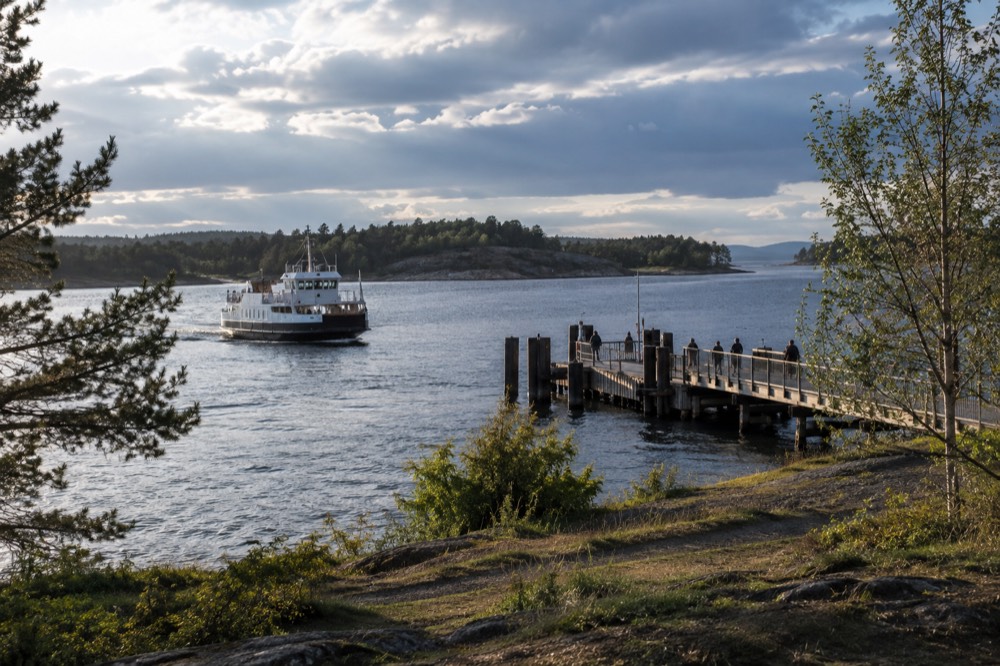 A ferry boat approaching a wooden pier on a green island in the Oslofjord