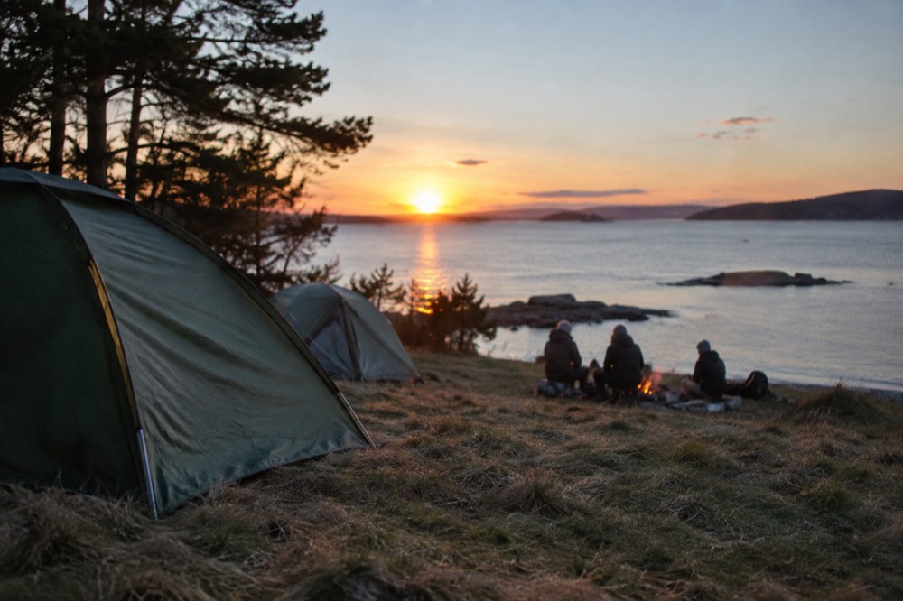 Tents pitched on open grassland near the shoreline at dusk