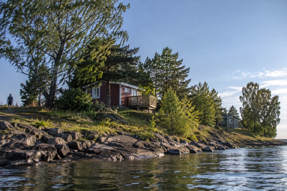 Small wooden holiday cabins on a green island shoreline dotted with trees