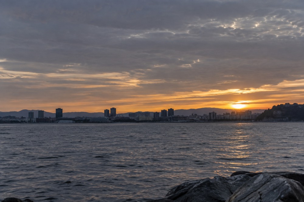 People-free view across open fjord water toward a distant city skyline at golden hour