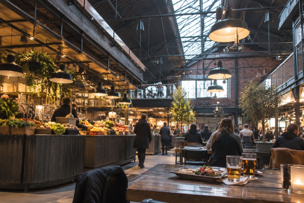 Communal wooden tables with trays of food and glasses of beer in a food hall