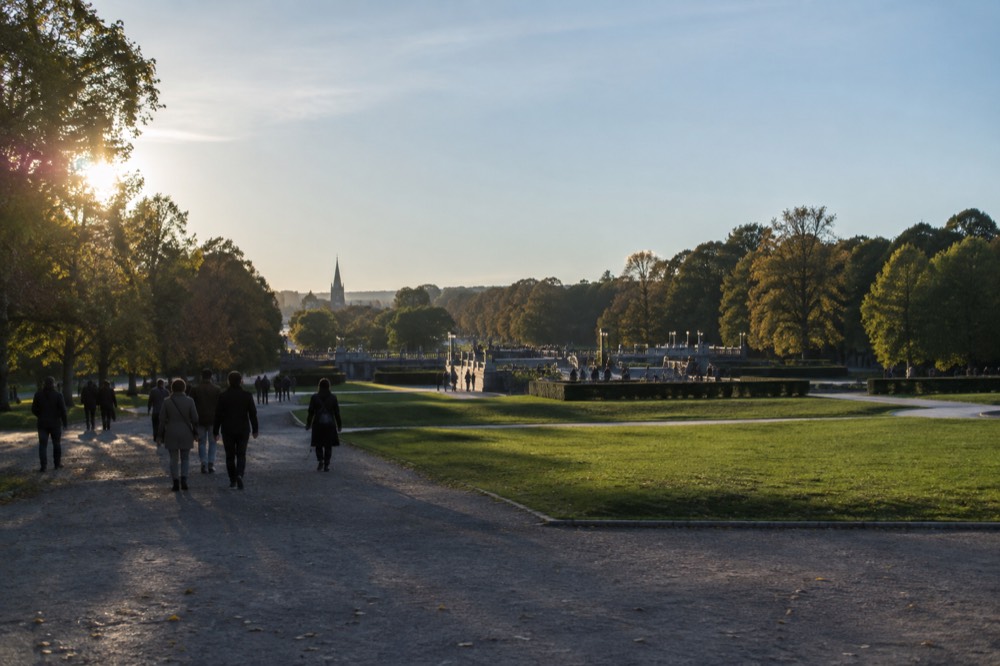 Visitors strolling gravel paths between green lawns in Vigeland Sculpture Park on a clear day